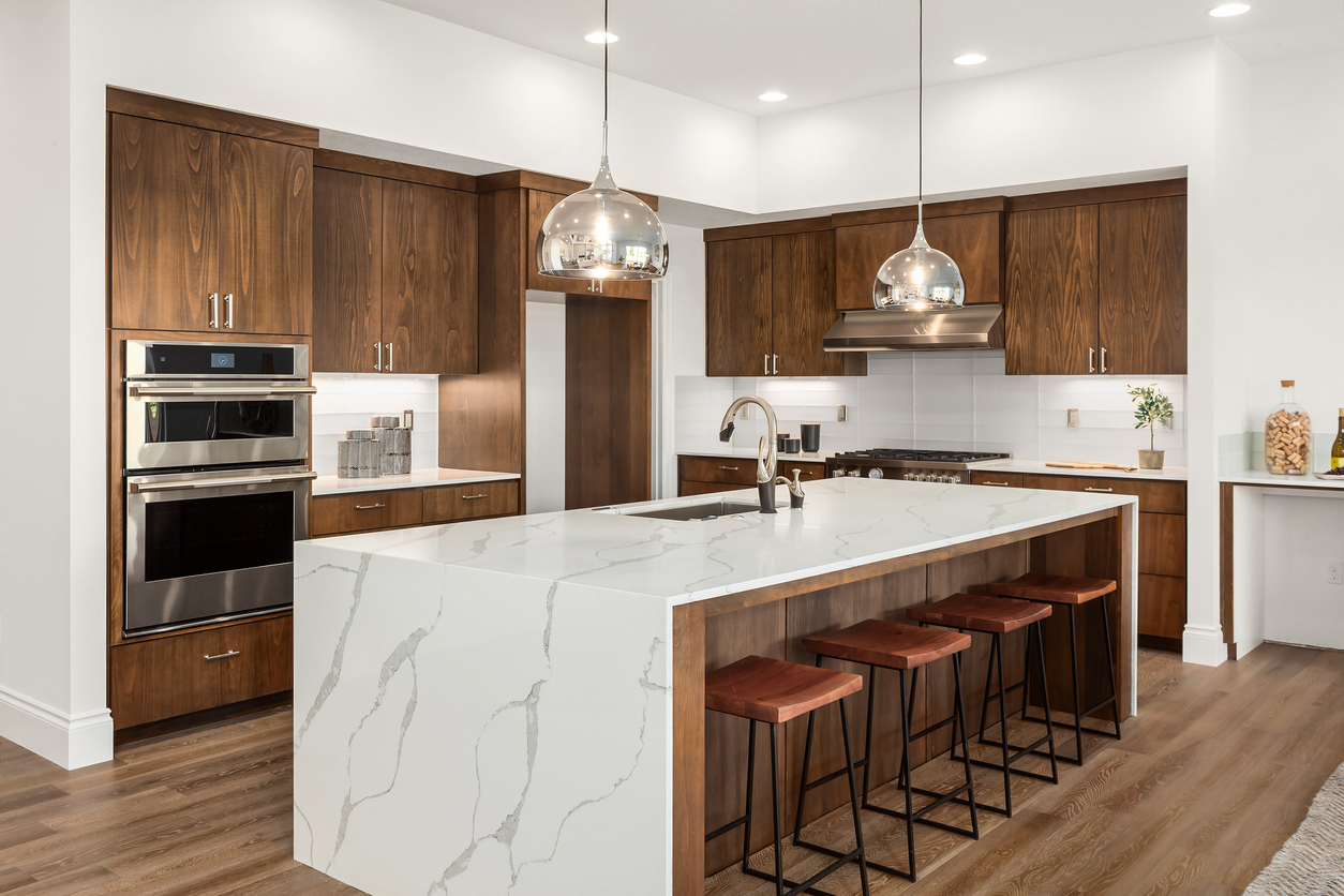 Beautiful kitchen in new luxury home with island, pendant lights, and hardwood floors. Features quartz waterfall island with dark cabinets and stainless steel appliances.